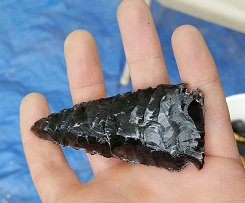 hand holding a flint-knapped arrowhead made from obsidian